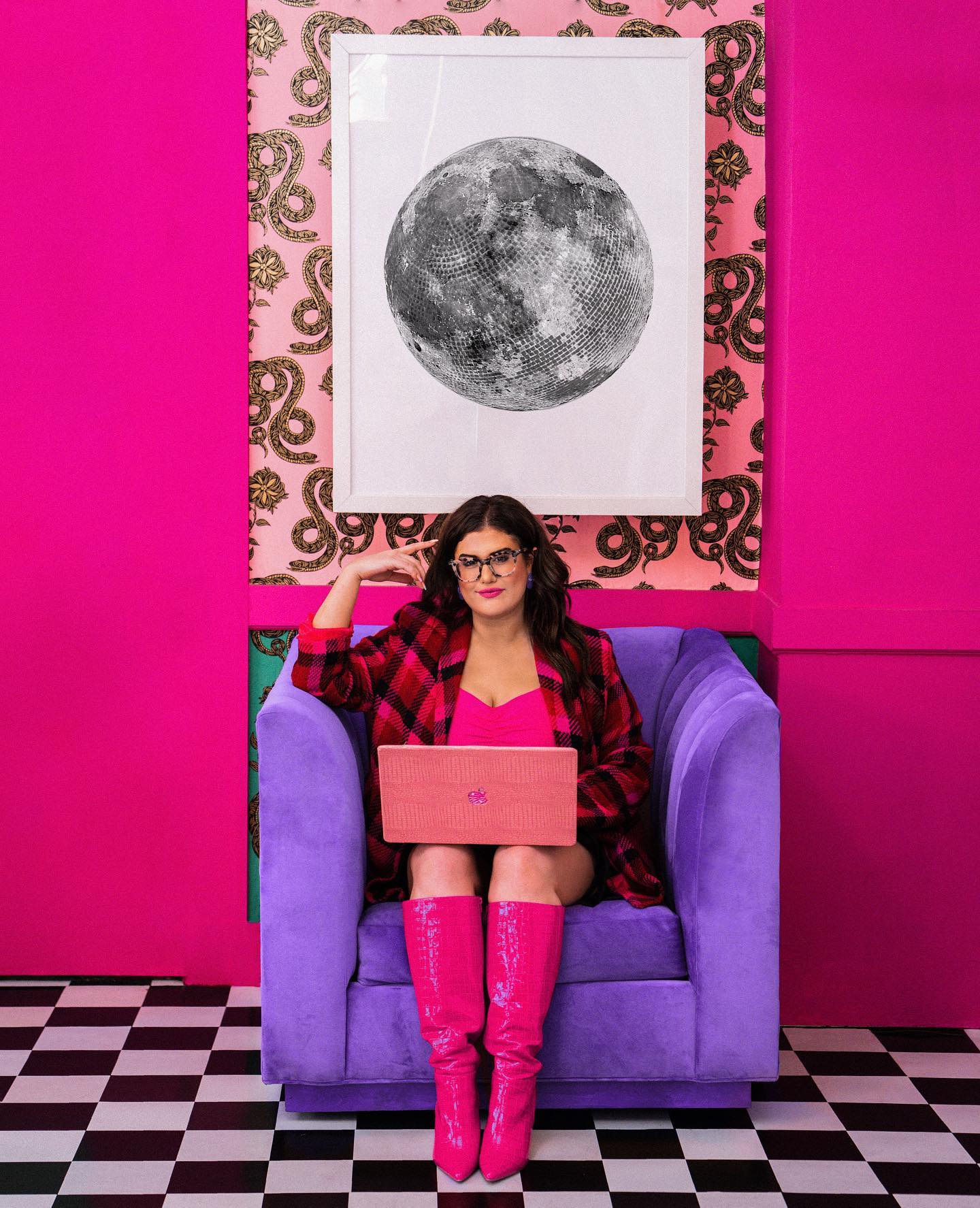 Hana Brenner-Katz, founder of Beyond Bright Creative, in a purple velvet chair in a hot pink room with a laptop