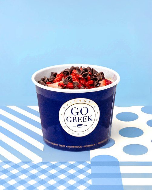 Go Greek Yogurt cup topped with berries on blue tile