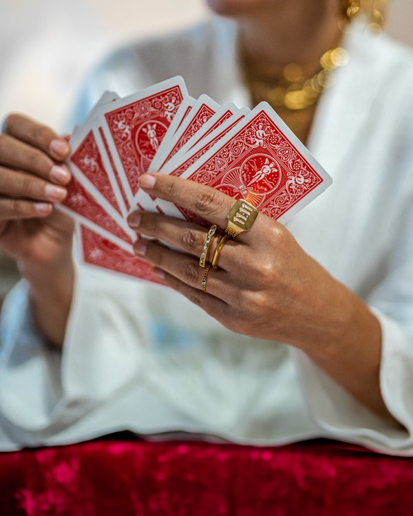 Nashrow photo: hands fanning playing cards, wearing gold rings and necklaces