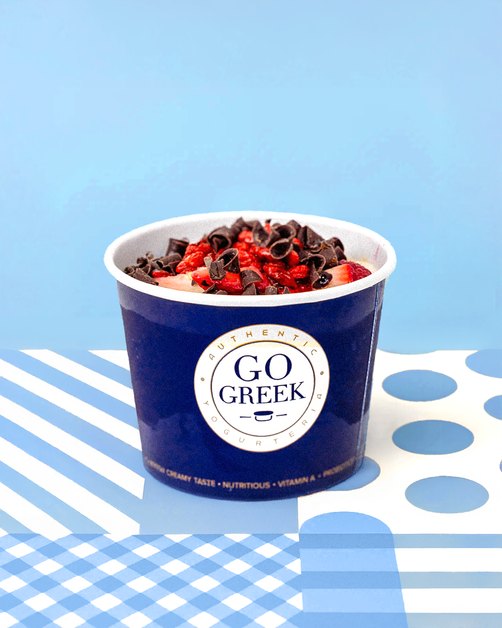 Go Greek Yogurt cup topped with berries on blue tile