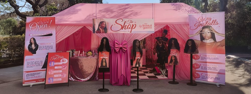 Pink branded booth with wigs on stands at an outdoor event